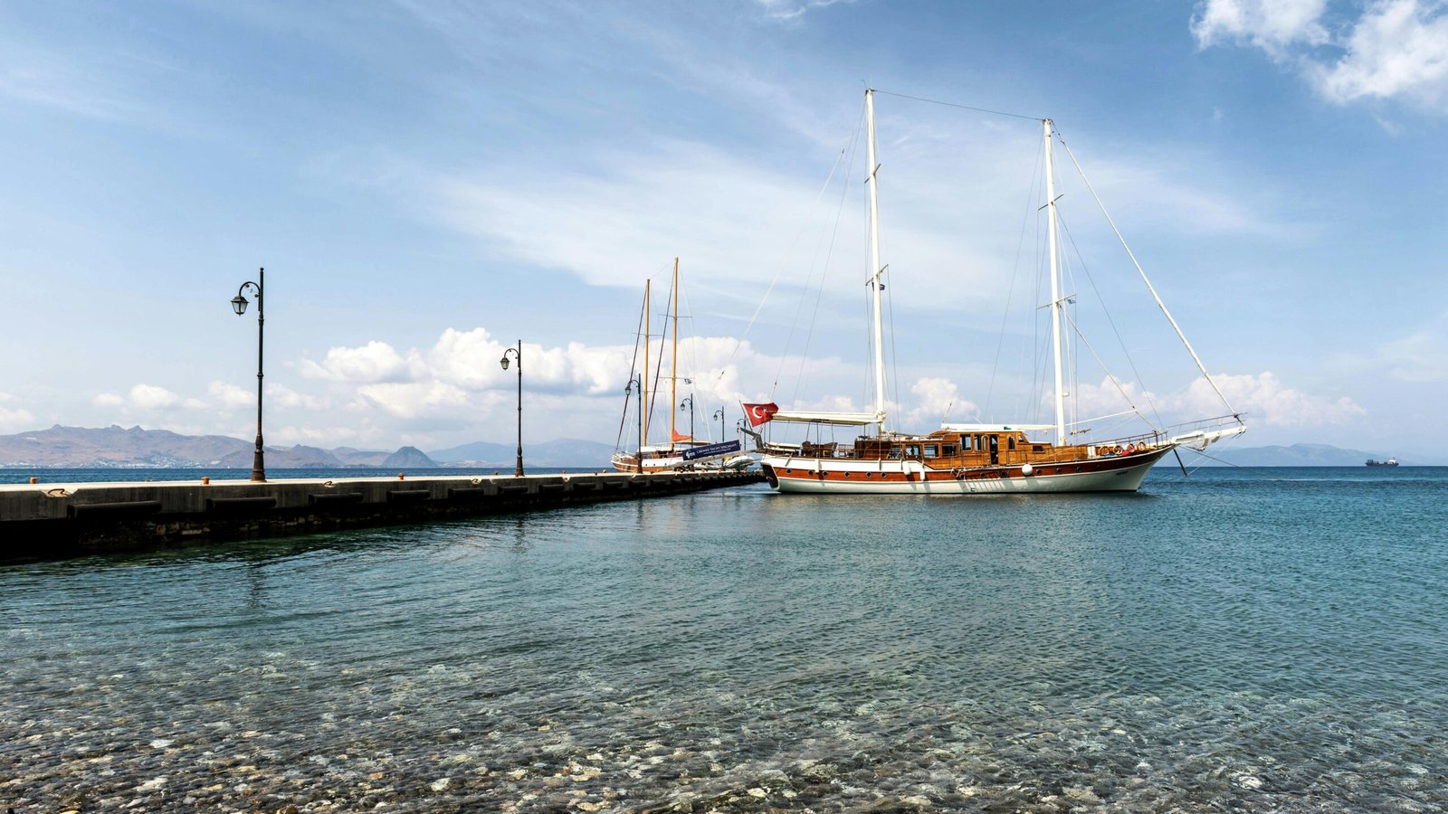 A serene view of a sailboat moored at a pier in Kos, Greece, under a clear blue sky.